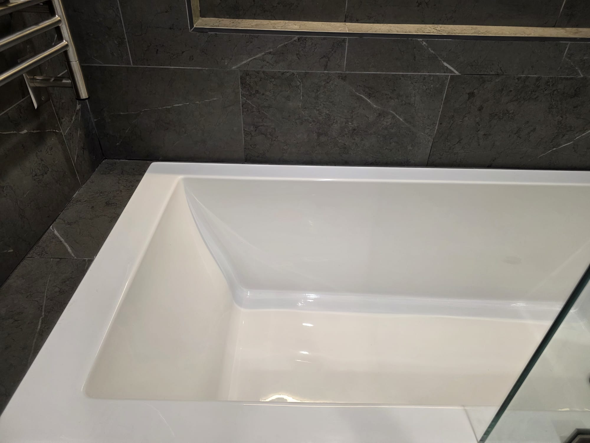 Bañera blanca rodeada de azulejos oscuros después de la limpieza de Goncan